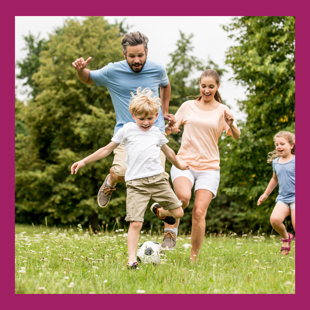 Parents playing football in a field with two young children